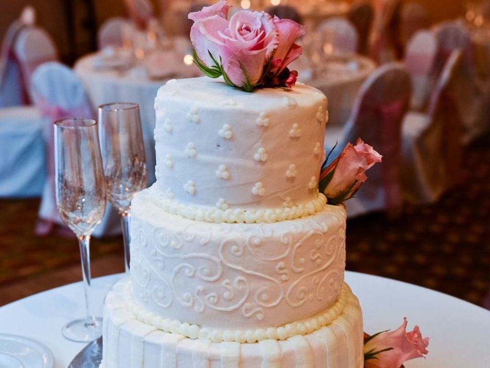 Tiered wedding cake with roses on top.
